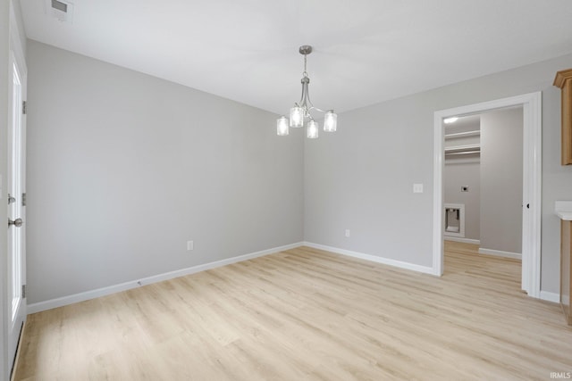 spare room with light wood-style flooring, a notable chandelier, visible vents, and baseboards