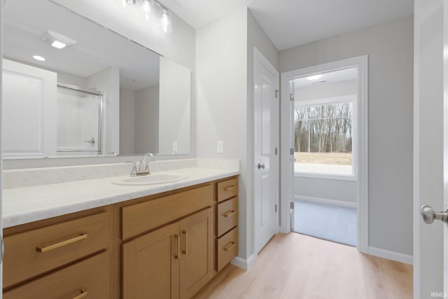 full bath with a shower with shower door, baseboards, wood finished floors, and vanity