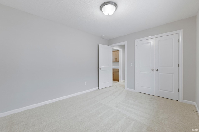 unfurnished bedroom featuring a closet, light colored carpet, a textured ceiling, and baseboards