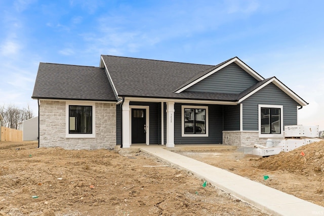 view of front facade featuring stone siding, a porch, and a shingled roof