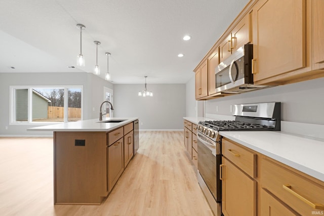 kitchen with light wood finished floors, light countertops, an island with sink, appliances with stainless steel finishes, and a sink