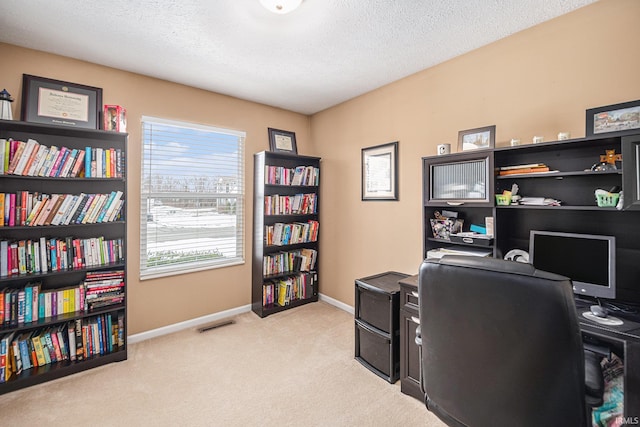 office area with a textured ceiling, visible vents, baseboards, and light carpet