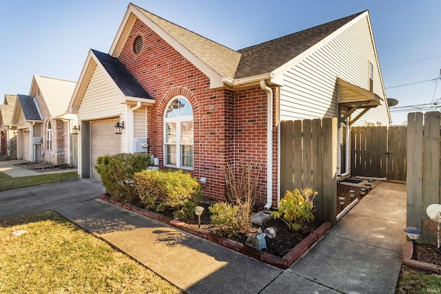 view of side of home with brick siding, a shingled roof, fence, concrete driveway, and a garage