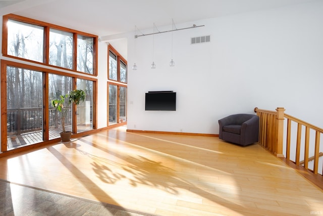 unfurnished living room with visible vents, baseboards, floor to ceiling windows, a high ceiling, and wood finished floors