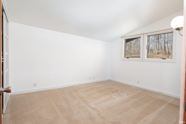 carpeted empty room featuring vaulted ceiling and baseboards