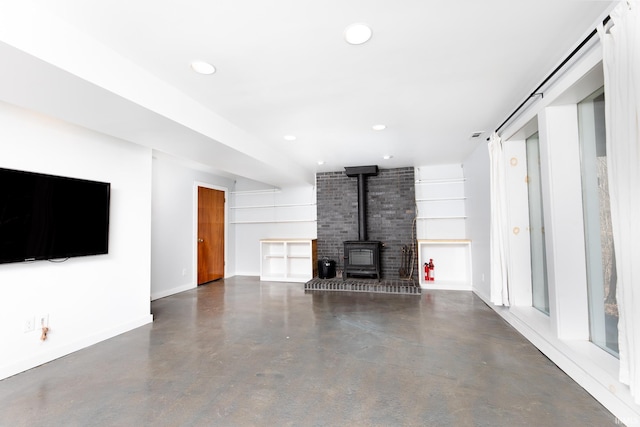 unfurnished living room with recessed lighting, concrete flooring, a wood stove, and baseboards