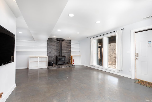 unfurnished living room featuring a wood stove, baseboards, visible vents, and finished concrete floors