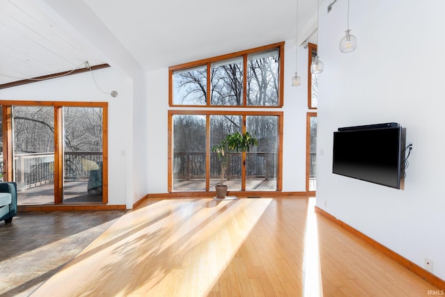 unfurnished living room with wood finished floors, baseboards, and high vaulted ceiling