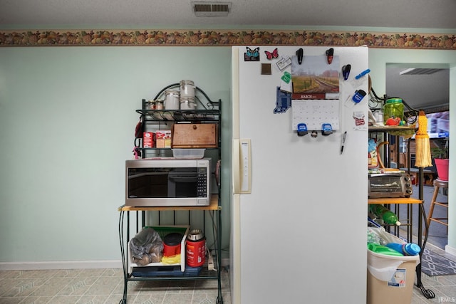 room details with visible vents, baseboards, stainless steel microwave, and freestanding refrigerator