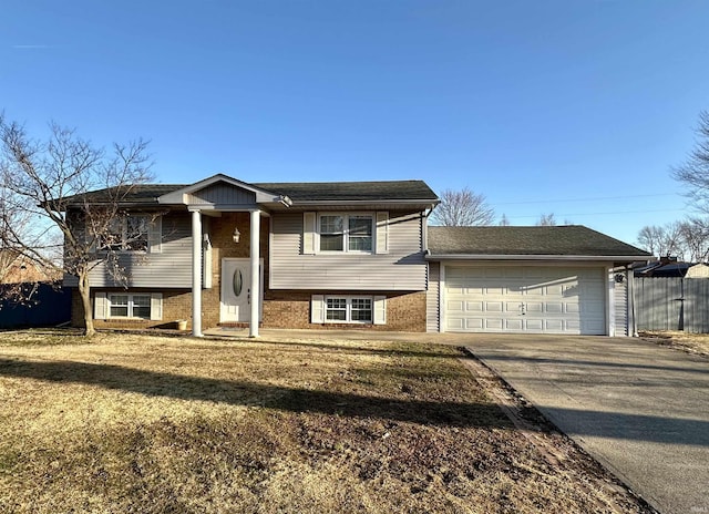 bi-level home featuring brick siding, an attached garage, fence, a front yard, and driveway