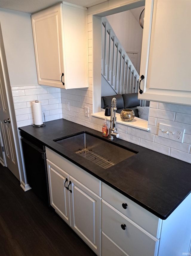 kitchen featuring white cabinetry, dark countertops, black dishwasher, and a sink