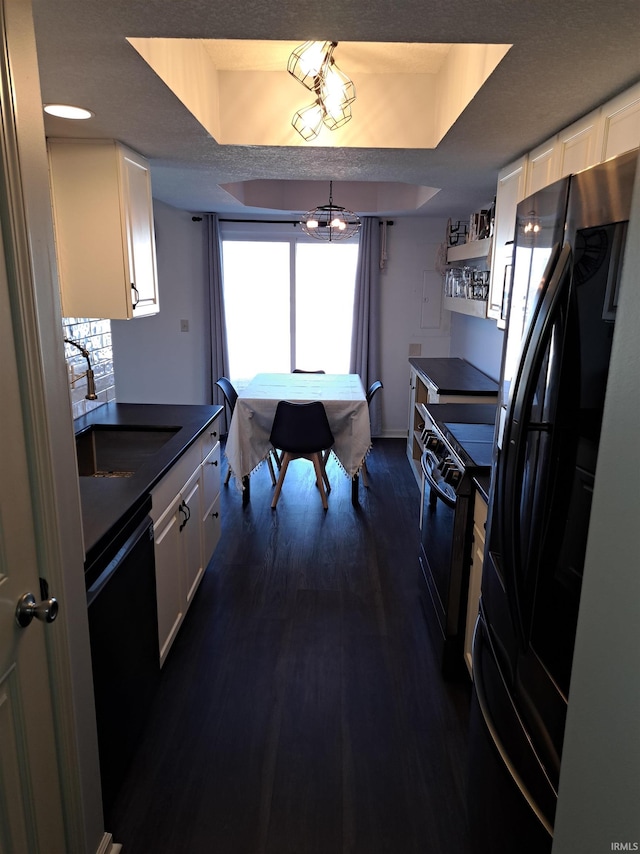 kitchen with white cabinets, black appliances, a raised ceiling, and a sink