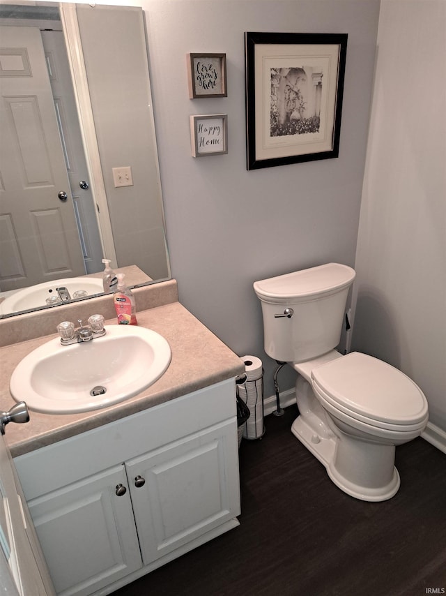 bathroom with toilet, vanity, baseboards, and wood finished floors