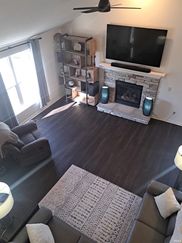 living area with lofted ceiling, wood finished floors, a stone fireplace, baseboards, and ceiling fan