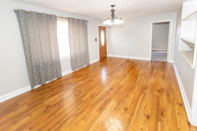 spare room featuring light wood finished floors, a notable chandelier, a textured ceiling, and baseboards