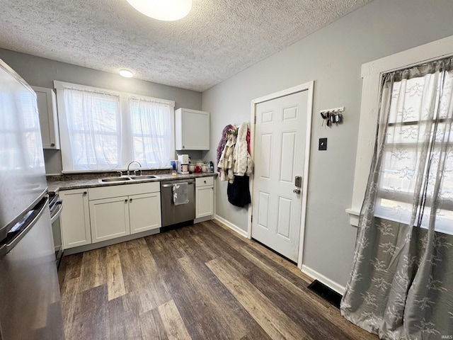 kitchen featuring dark wood-type flooring, a sink, appliances with stainless steel finishes, white cabinets, and baseboards