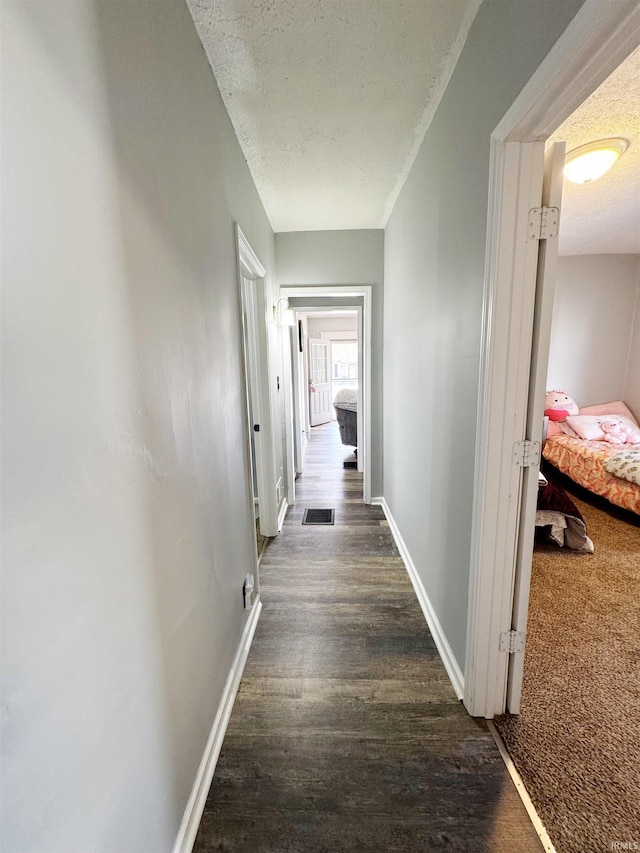 corridor with visible vents, baseboards, a textured ceiling, and wood finished floors