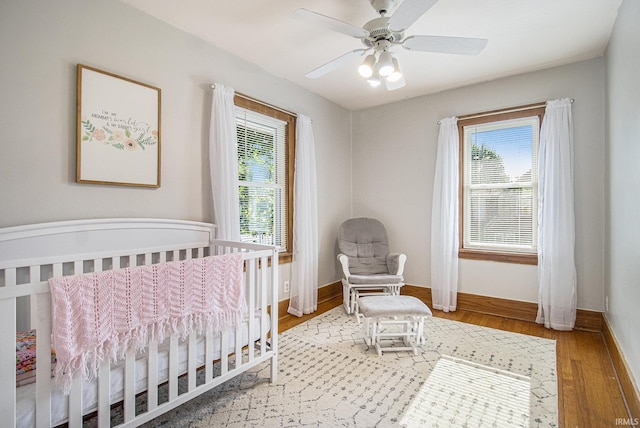 bedroom featuring ceiling fan, a crib, baseboards, and wood finished floors