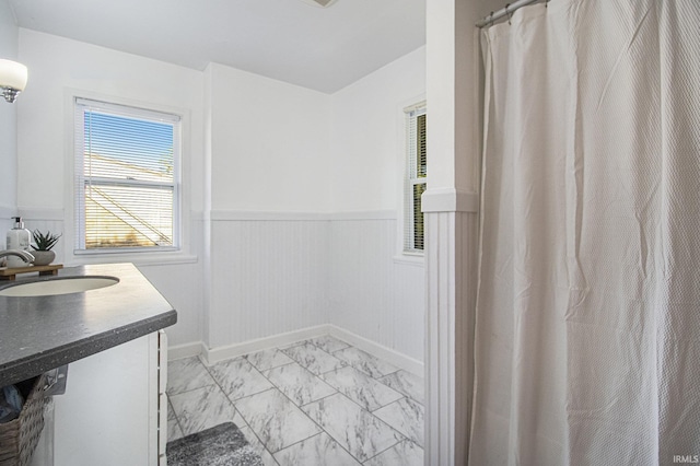 full bathroom featuring a sink, a wainscoted wall, and marble finish floor