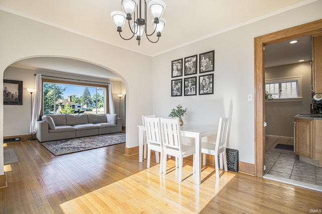 dining room with wood-type flooring, arched walkways, an inviting chandelier, and ornamental molding