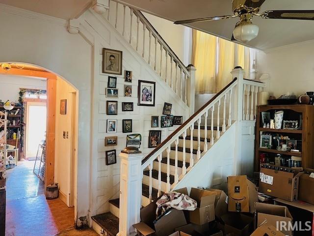 stairway with wood finished floors, arched walkways, ornamental molding, and a ceiling fan