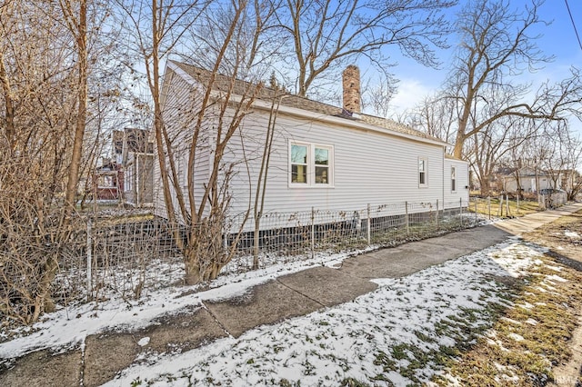 view of snow covered exterior featuring a shingled roof, a chimney, and fence