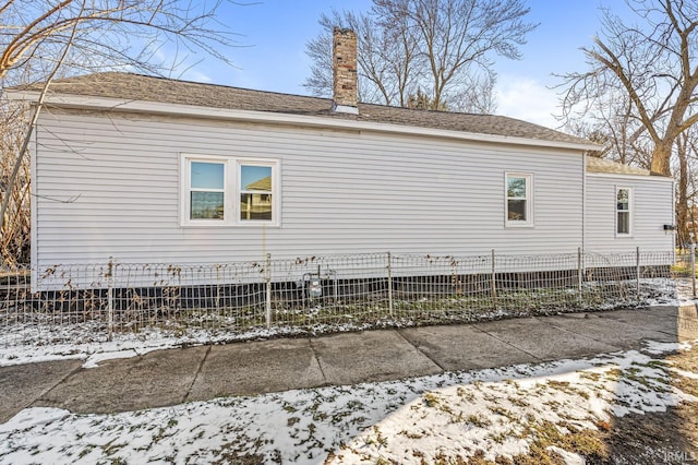 view of home's exterior featuring a chimney, roof with shingles, and fence