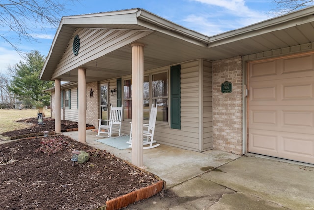 doorway to property with brick siding, a porch, and a garage