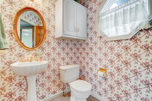 half bath with toilet, wallpapered walls, and baseboards