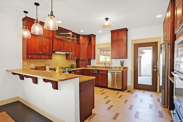 kitchen with decorative light fixtures, appliances with stainless steel finishes, a peninsula, and reddish brown cabinets