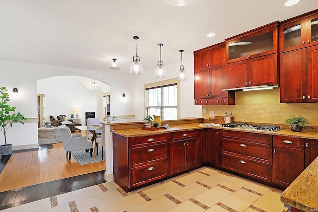 kitchen with arched walkways, dark brown cabinets, a peninsula, and stainless steel gas cooktop