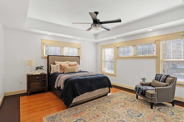 bedroom with a raised ceiling, wood finished floors, and baseboards