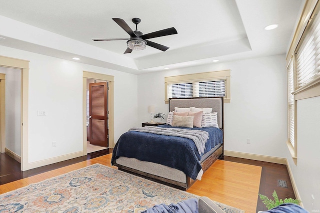 bedroom featuring a raised ceiling, multiple windows, and wood finished floors