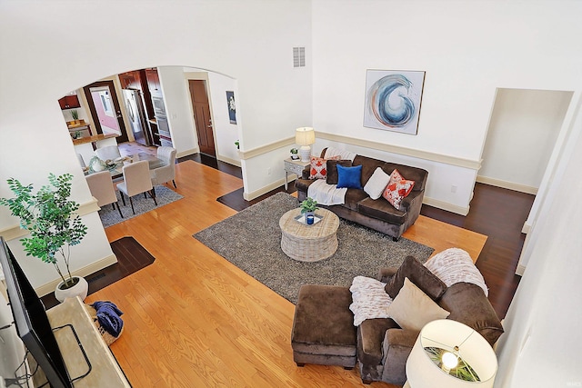 living area with arched walkways, visible vents, baseboards, and wood finished floors