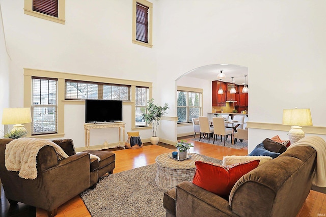 living room featuring baseboards, arched walkways, light wood-style floors, and a high ceiling