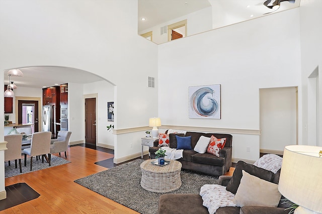 living room with visible vents, light wood-style flooring, arched walkways, a high ceiling, and baseboards