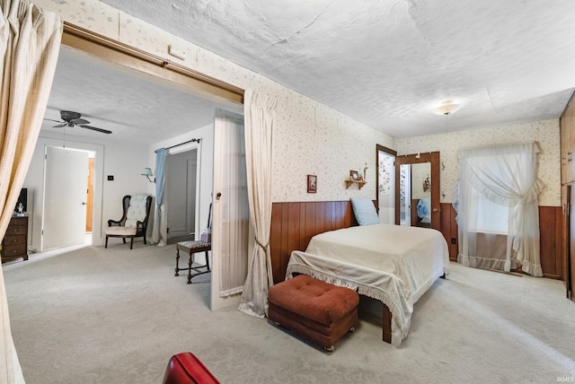 carpeted bedroom featuring a wainscoted wall, a textured ceiling, and wallpapered walls