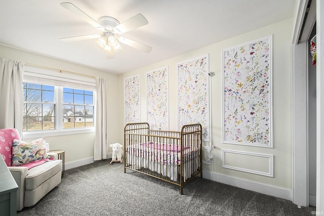 bedroom featuring a nursery area, baseboards, carpet, and a ceiling fan