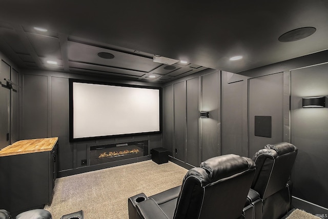 home theater room with a decorative wall, carpet, and a glass covered fireplace