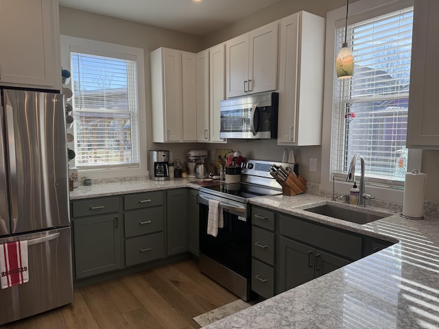 kitchen featuring a sink, stainless steel appliances, light stone countertops, and wood finished floors