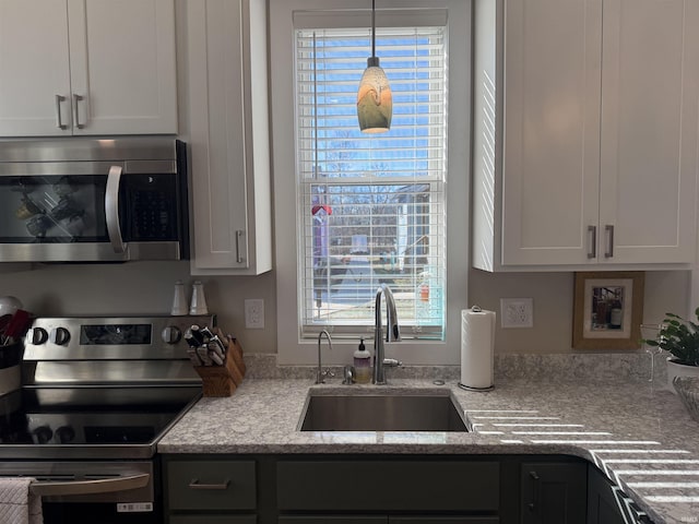 kitchen with light stone countertops, decorative light fixtures, white cabinets, stainless steel appliances, and a sink