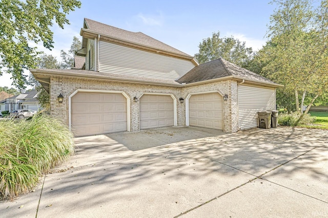 view of side of property featuring brick siding, driveway, an attached garage, and roof with shingles