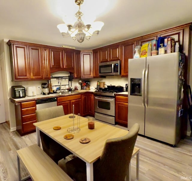 kitchen featuring a chandelier, light wood-style flooring, hanging light fixtures, stainless steel appliances, and a sink