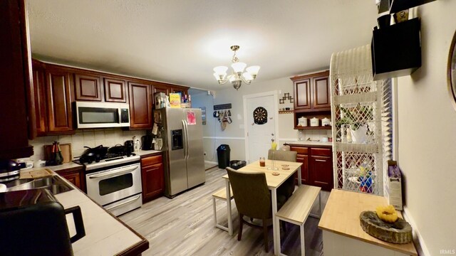 kitchen featuring an inviting chandelier, a sink, light countertops, light wood-style floors, and appliances with stainless steel finishes