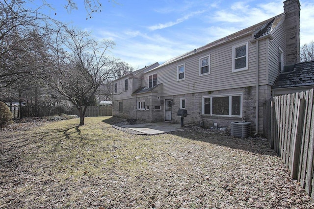 rear view of house with central AC unit, a lawn, a chimney, a fenced backyard, and a patio