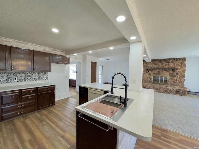 kitchen with arched walkways, a stone fireplace, light countertops, dark brown cabinetry, and dishwasher