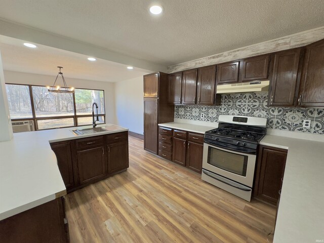 kitchen with stainless steel range with gas cooktop, under cabinet range hood, light countertops, light wood-style floors, and a sink