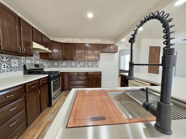 kitchen featuring stainless steel gas range oven, light wood finished floors, backsplash, under cabinet range hood, and arched walkways