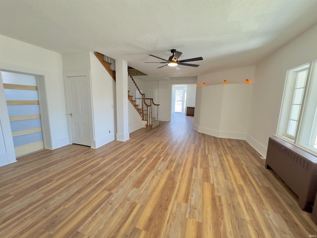 unfurnished room with stairs, radiator, light wood-type flooring, and a textured ceiling