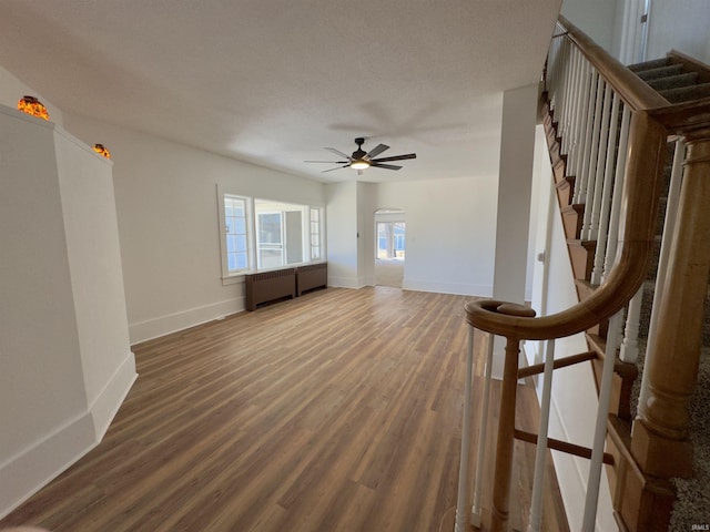 unfurnished living room with stairs, wood finished floors, baseboards, and a ceiling fan